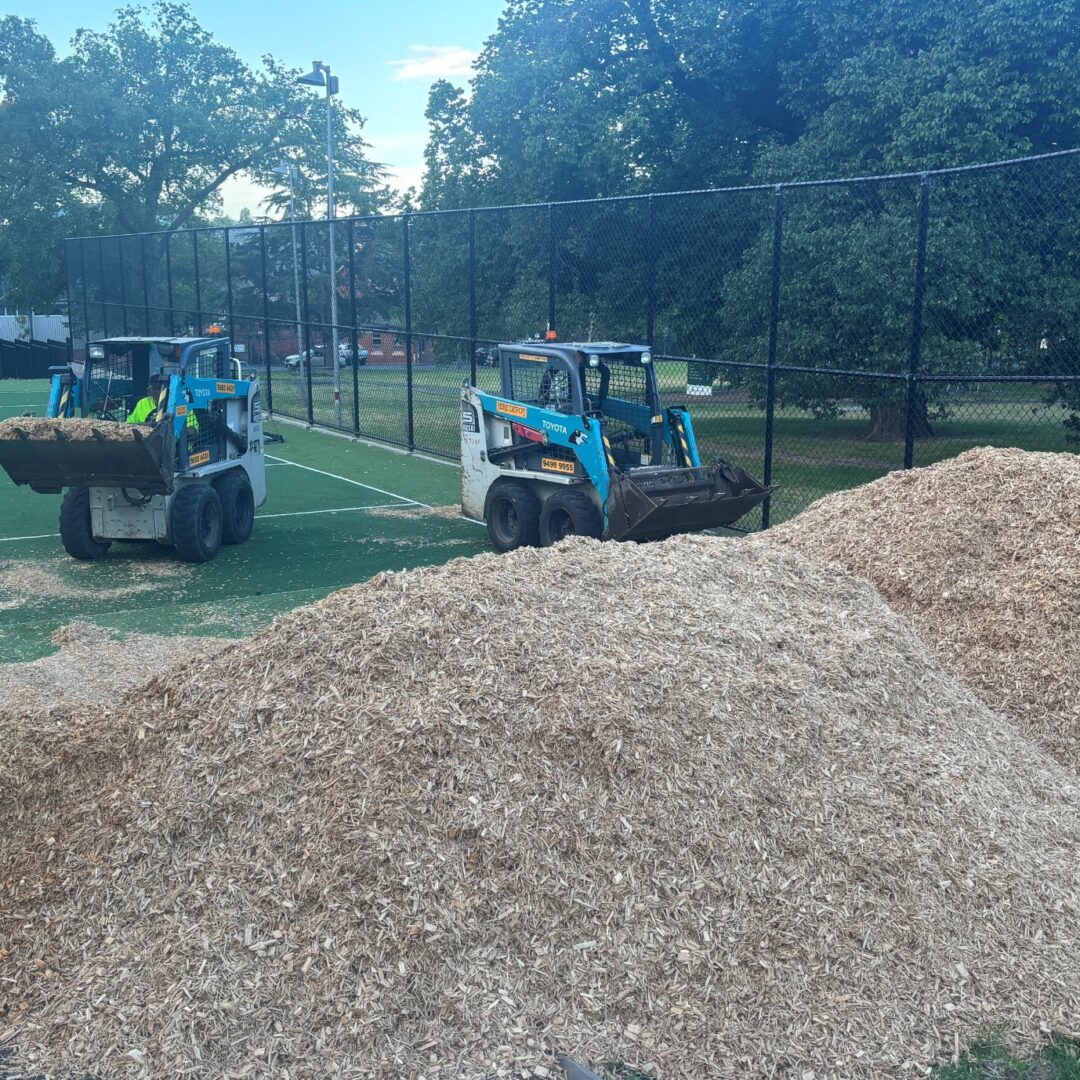 Skid steers spreading wood chips on turf