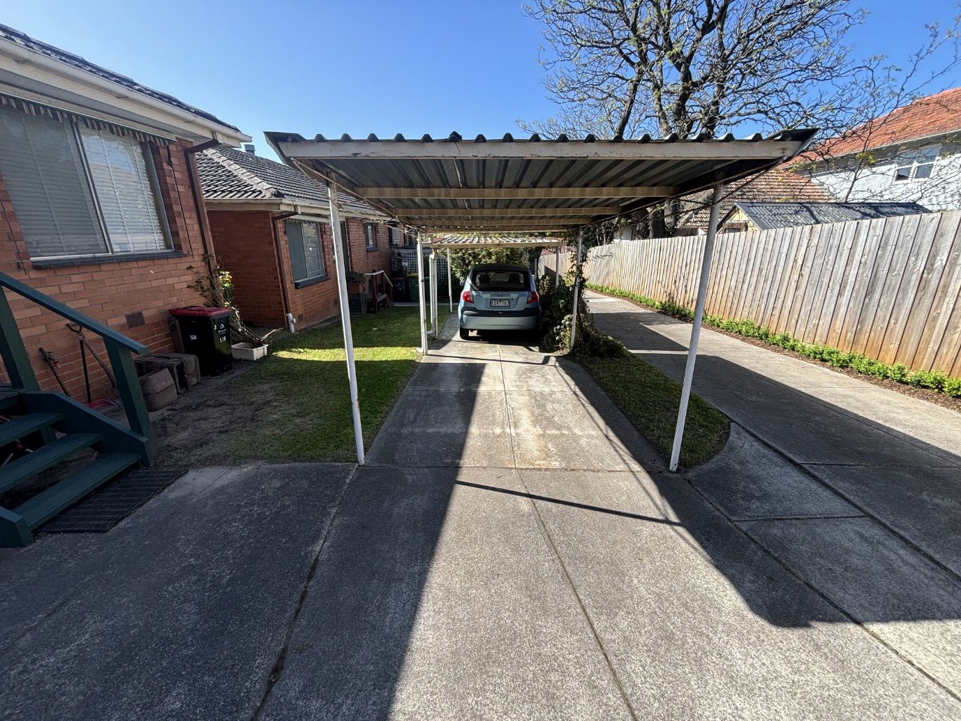 Car parked beneath metal carport between houses