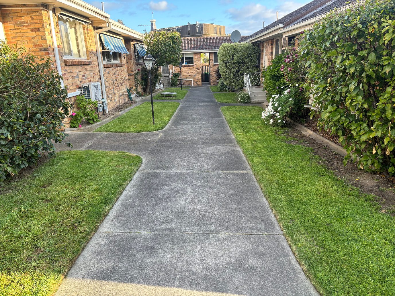 Concrete walkway between brick rowhouses with lawns